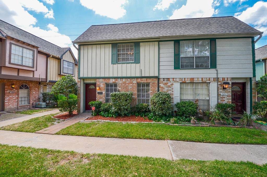 This photo shows a charming two-story townhouse with a brick and siding exterior. It features green shutters, a well-maintained front yard with shrubs, and a pathway leading to the entrance. The neighborhood appears tidy and inviting.