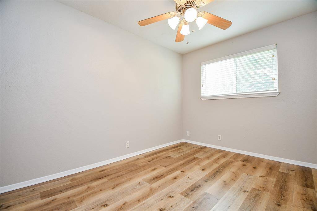 This room features a neutral color palette with light gray walls and wood-style flooring. It has a ceiling fan and a window that lets in natural light, creating a bright and airy space.