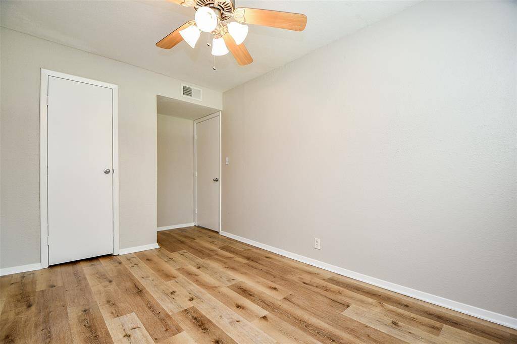This room features fresh light-colored walls, wood-style flooring, a ceiling fan with lights, and two doors, perfect for a cozy bedroom or home office.