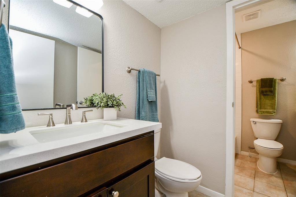 This bathroom features a modern vanity with a sleek countertop and a large mirror. It has neutral-colored walls, tile flooring, and an adjacent toilet area, creating a clean and functional space.