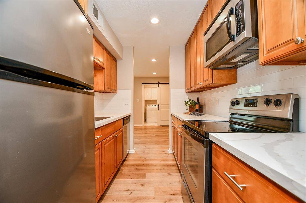 This kitchen features modern stainless steel appliances, warm wood cabinetry, and sleek countertops. The space is well-lit with recessed lighting and offers a cozy, efficient layout.