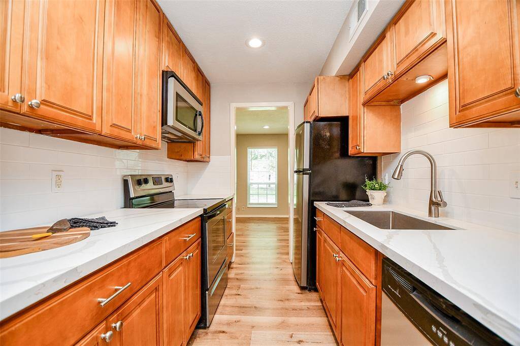 This kitchen features warm wood cabinetry, modern stainless steel appliances, and sleek white countertops. It's well-lit with recessed lighting and has a clean, contemporary design.