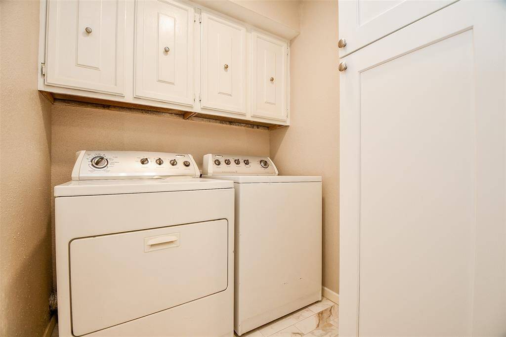 Compact laundry room with a washer and dryer, featuring overhead cabinets for storage, all in a neutral color scheme.