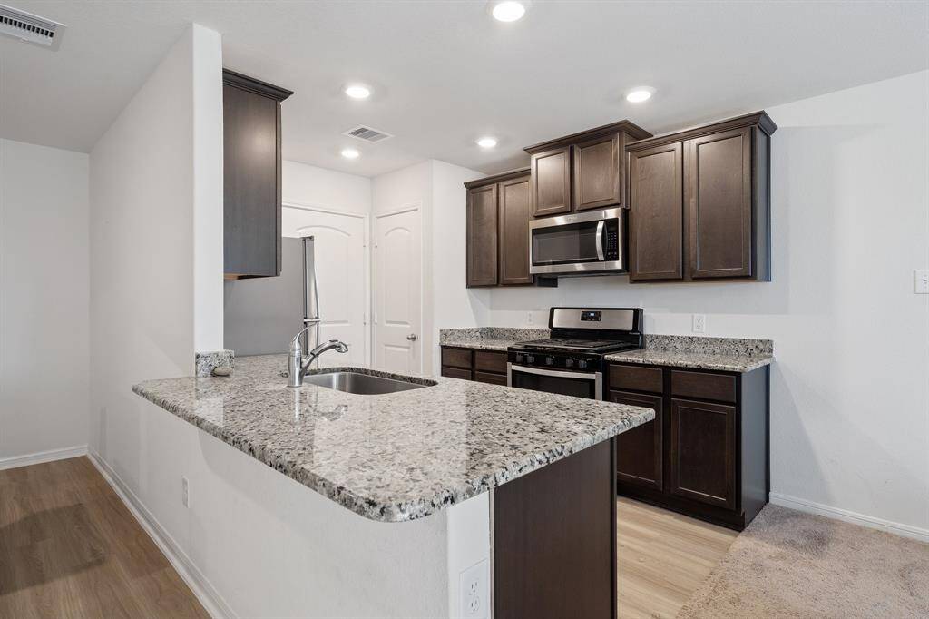 This light and bright kitchen features a large granite island, dark stained cabinets, a large sink overlooking your family room, & recessed lighting.