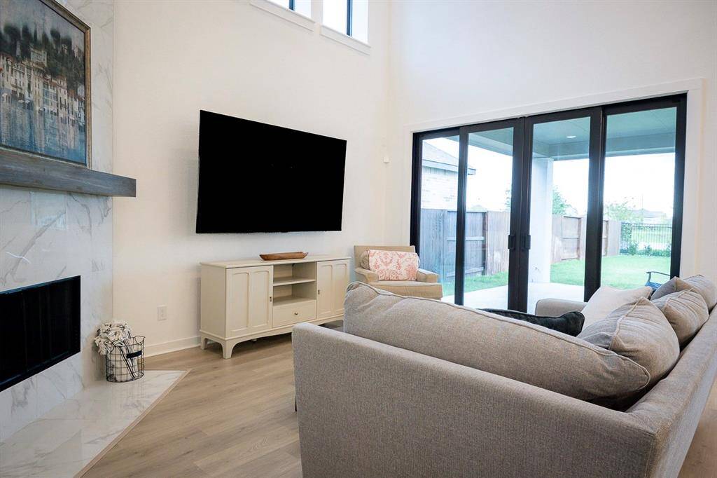 Spacious and inviting living area featuring a cozy fireplace, sleek flooring, and abundant natural light from expansive sliding doors leading to the backyard. Perfect for relaxing and entertaining.