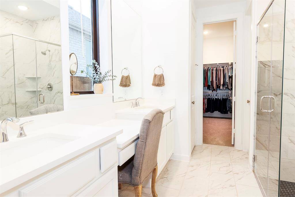 Luxurious primary bathroom featuring elegant marble flooring, a spacious glass-enclosed shower, and a convenient vanity area. Direct access to a walk-in closet enhances functionality and style.