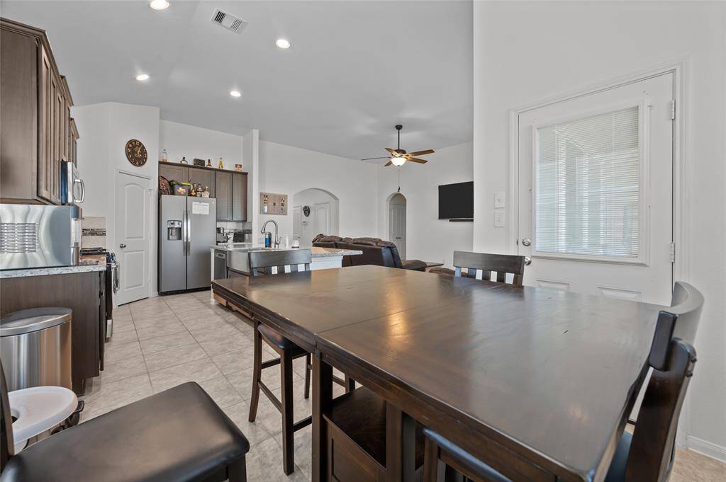 This open-concept kitchen and dining area features modern appliances, ample cabinetry, and a spacious countertop. It flows seamlessly into a cozy living room with a ceiling fan and wall-mounted TV, providing a welcoming atmosphere for family gatherings. The neutral color palette and tiled flooring add a touch of elegance and ease of maintenance.