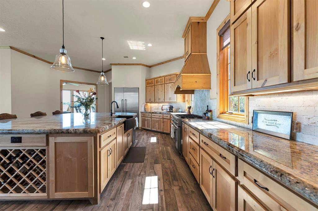 Show off your culinary skills in this warm and inviting kitchen, where rich granite countertops, tumbled stone backsplash, and sleek stainless steel appliances blend seamlessly with custom cabinetry and a statement wood vent hood. The oversized island is perfect for casual dining and gathering with guests, while under-cabinet lighting and a spacious butler’s pantry enhance both the functionality and charm of this thoughtfully designed space.