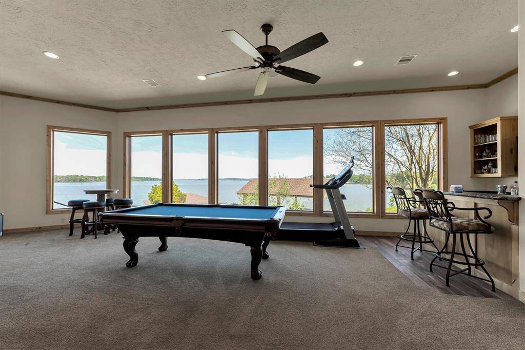 Just off the kitchen and dining area, this spacious game room offers the perfect retreat for fun and relaxation. Enjoy a built-in bar with a wet bar setup, plenty of space for games and activities, and a wall of windows showcasing breathtaking views of the lake.