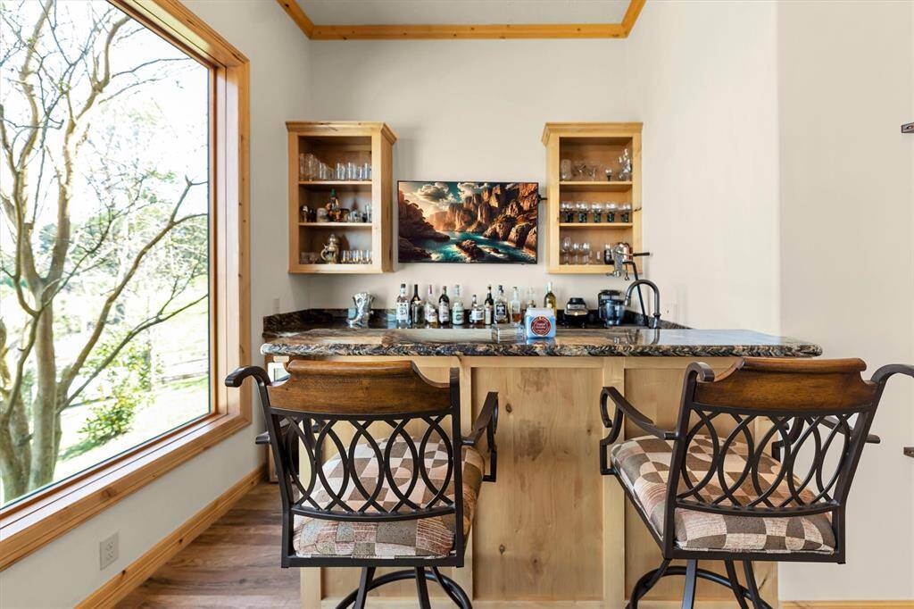 The game room bar offers the perfect setup for entertaining, featuring granite countertops, bar seating, custom shelving and storage, a built-in sink, and a convenient drink chiller—everything you need to keep the good times flowing.