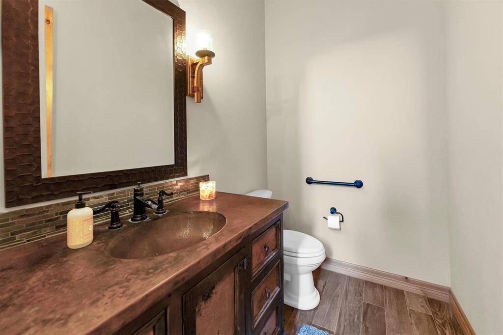 There’s nothing boring about this half bath—rustic charm and unique details steal the show. A rich wood vanity with a copper countertop and sink pairs beautifully with a hammered copper-framed mirror, while a warm wall-mounted sconce adds the perfect touch of ambient lighting.