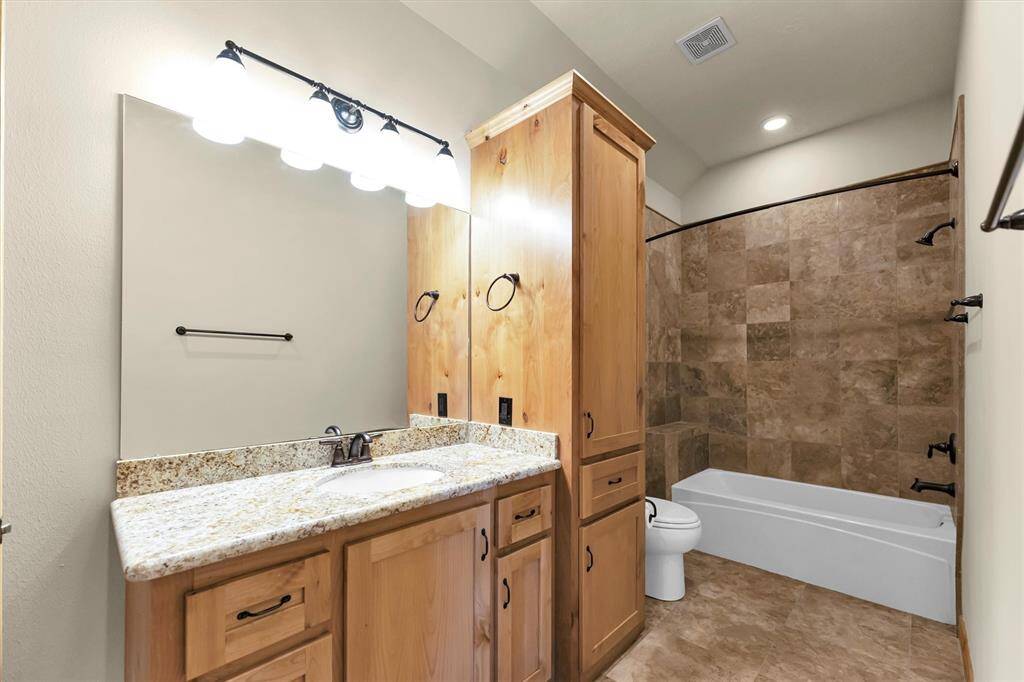 This spotless ensuite bathroom offers a single sink vanity, linen storage, and a beautifully tiled tub/shower enclosure with a bench.