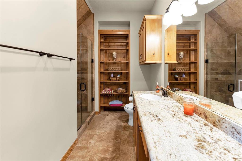 Beautifully appointed for guests, this private ensuite features an expansive single-sink vanity, custom shelving, and a spacious walk-in shower with a bench, elegant tilework, and frameless glass. Comfort and style come together to create a welcoming retreat they'll appreciate.
