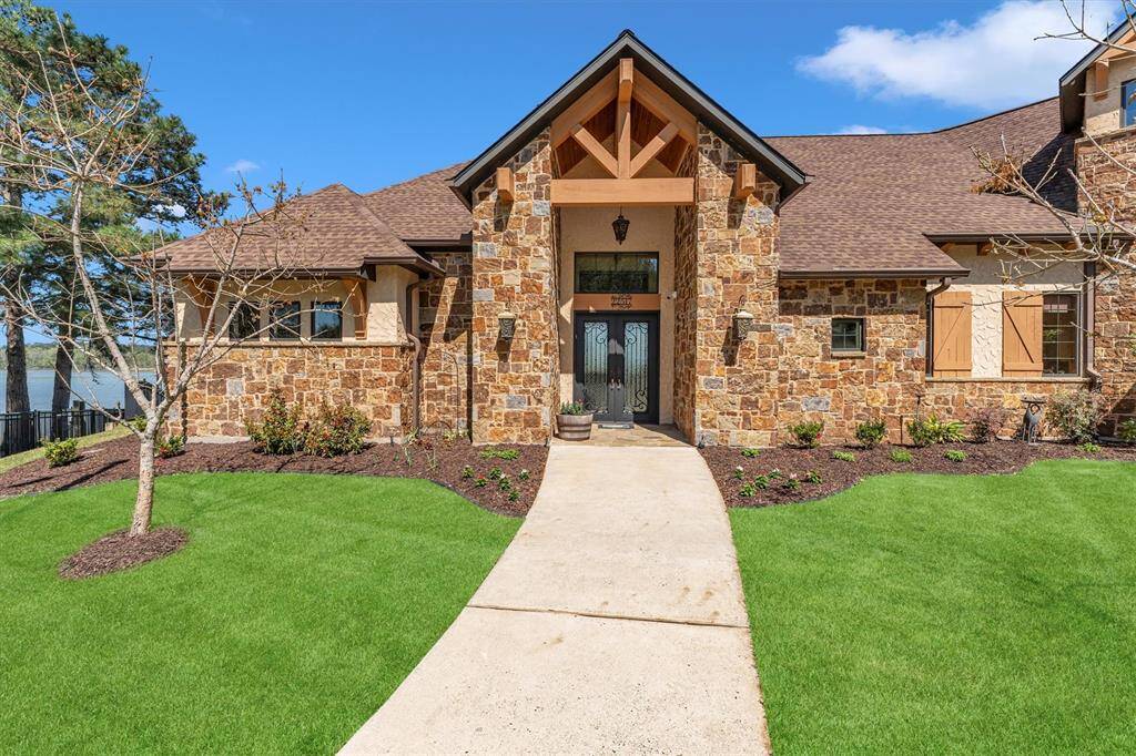 Welcome guests in style through this striking entry, where double leaded-glass doors set into a gorgeous stone façade make a lasting first impression. A peaked gable with exposed wood trusses and elegant lantern-style sconces add warmth and architectural charm, hinting at the high-end details found throughout the home.