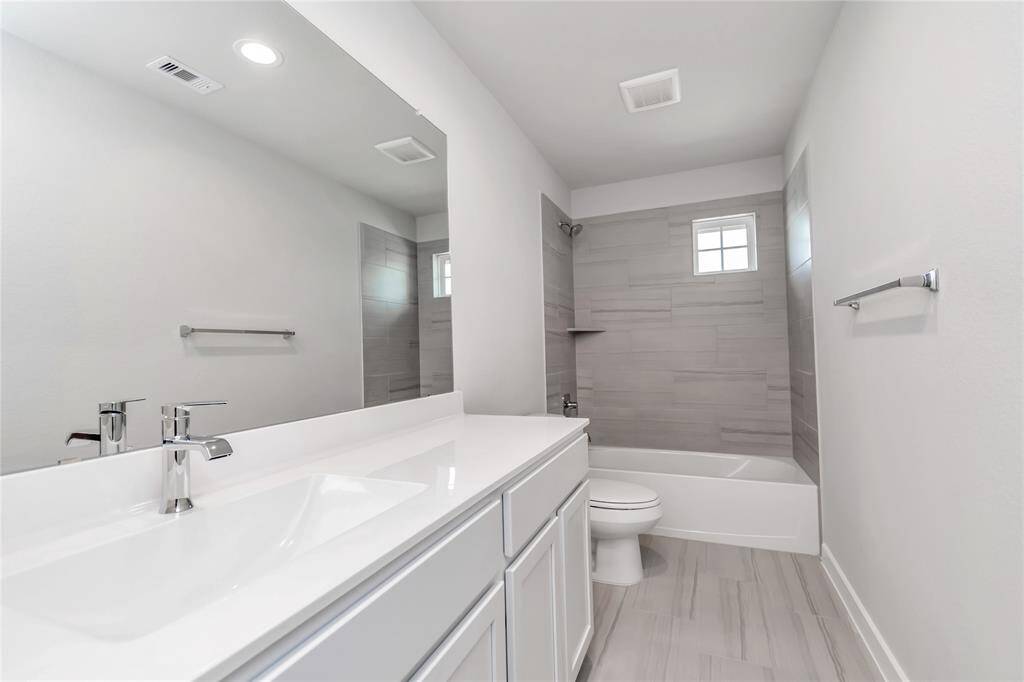 Indulge in refined charm in the secondary bathroom, where the tile flooring harmonizes with a bath/shower combo surrounded by tasteful tile. Light wood cabinets, coupled with a gorgeous countertop, elevate the space, cultivating a truly welcoming atmosphere. Sample photo of completed home with similar floor plan. As-built interior colors and selections may vary