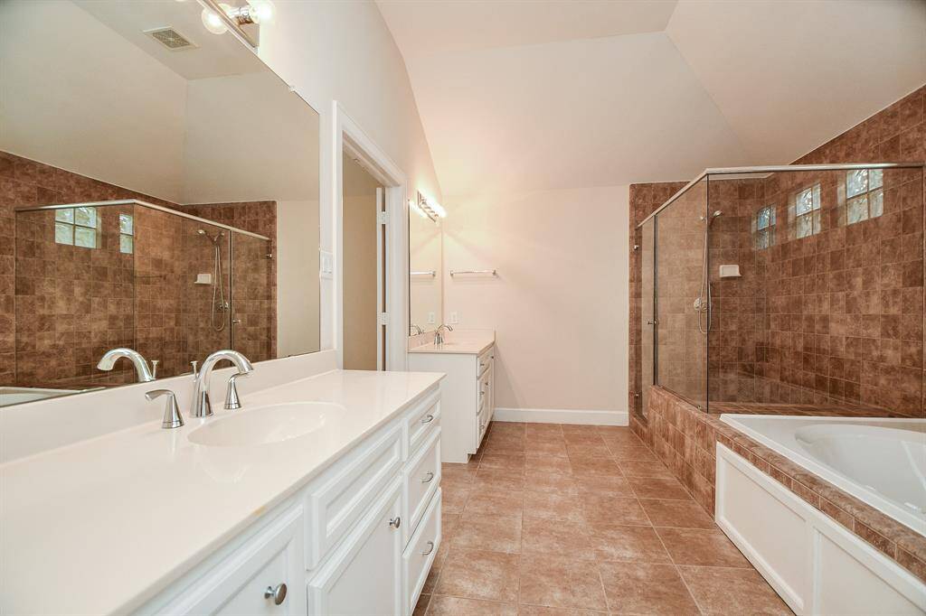Dynamic copper colored tile fills the oversized walk-in, glass enclosed shower (with stone bench inside), as it sits right next to the huge, jetted garden tub. Dual/separate sinks sit in snow white cabinetry/countertops, with shining wall-wide mirrors, above.