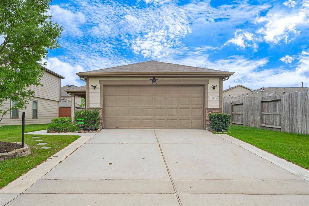 This photo shows a single-story home with a two-car garage, neatly maintained front yard, and a concrete driveway. The exterior features neutral siding and some landscaping, with a fenced backyard. The sky is clear and blue, adding to the inviting feel.