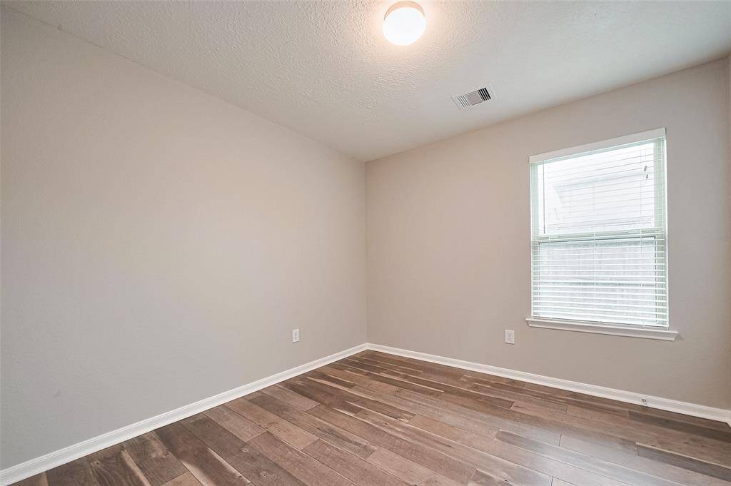 This photo shows a small, bright room with neutral-colored walls, wood flooring, and a single window allowing natural light. Ideal for a bedroom or office.