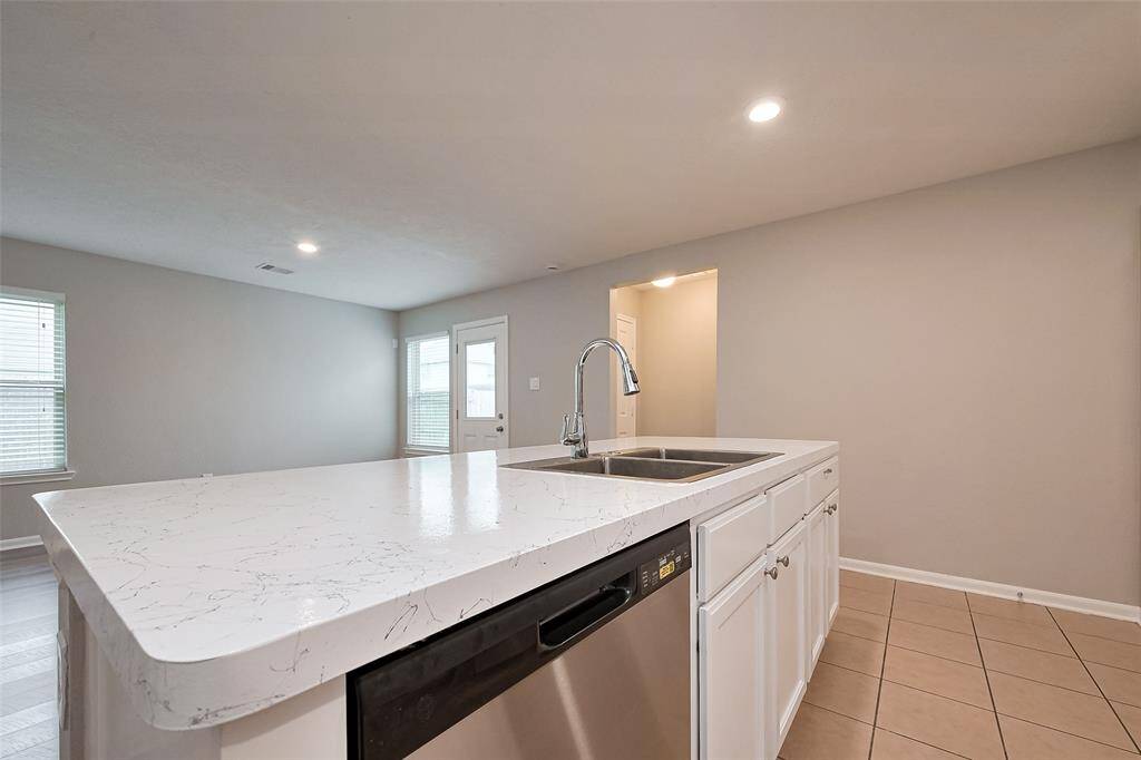 Modern kitchen with a spacious island featuring a sleek marble countertop and built-in sink. The open layout is enhanced by recessed lighting, neutral tones, and natural light from nearby windows.