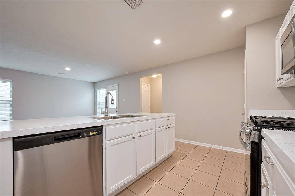 This modern kitchen features sleek white cabinetry, a spacious island with a sink, stainless steel appliances, and recessed lighting, creating a bright and functional space.