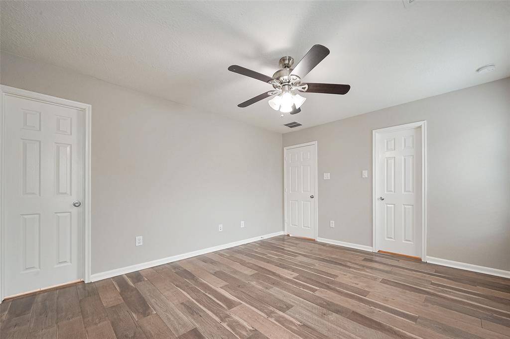 This room features neutral walls, wood-look flooring, and a ceiling fan with lights. It has multiple doors suggesting ample storage or access to other areas. Bright and airy, ideal for a bedroom or office.