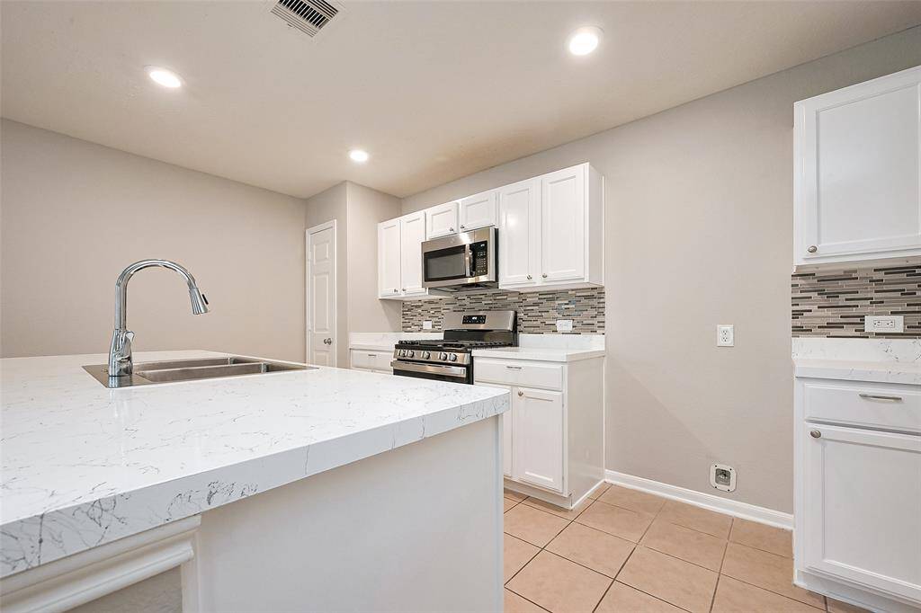This modern kitchen features sleek white cabinetry, a stylish tile backsplash, and stainless steel appliances. The spacious countertop with a built-in sink offers ample workspace, and the recessed lighting provides a bright, inviting atmosphere.