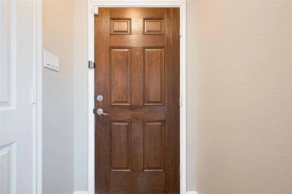 This photo features a classic wooden front door with a rich finish, set in a neutral-colored hallway. The door has a peephole and a modern lock and handle, offering a welcoming and secure entrance.