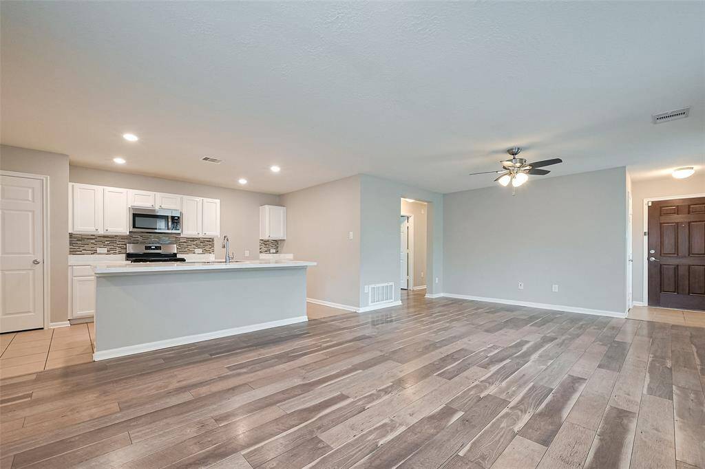 This photo showcases a modern, open-concept living space with a spacious kitchen featuring a large island, stainless steel appliances, and tiled backsplash. The living area has wood-look flooring, neutral walls, and a ceiling fan, creating a bright and inviting atmosphere.