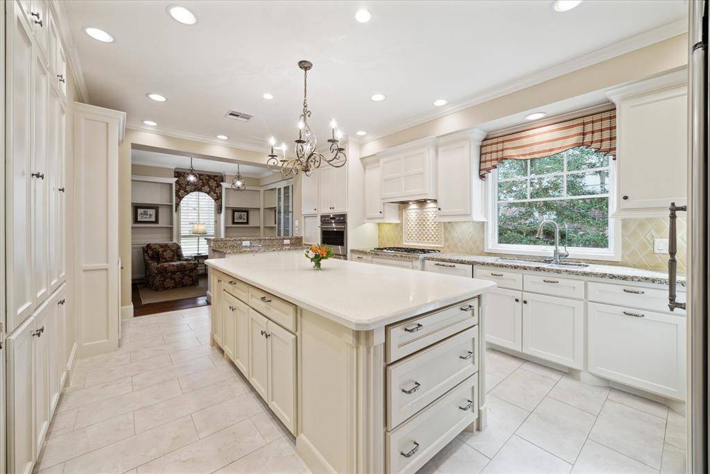 This angle captures the oversized window spanning above the sink. Recessed can lighting provides an abundance of task lighting, while the chandelier is like a piece of beautiful jewelry. Note the substantial storage provided in this well-designed island.