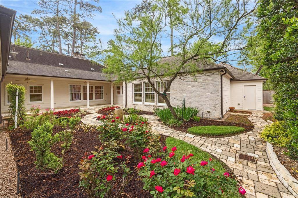 The charming backyard features a well-maintained garden with vibrant flowers, lush greenery, and an elegant water fountain. A stone pathway leads to a cozy patio area, perfect for relaxation. The exterior of the house is a blend of slurried brick and cement board siding, complemented by large windows and a welcoming ambiance.  Also, note to the right-hand side is a door to the garage.