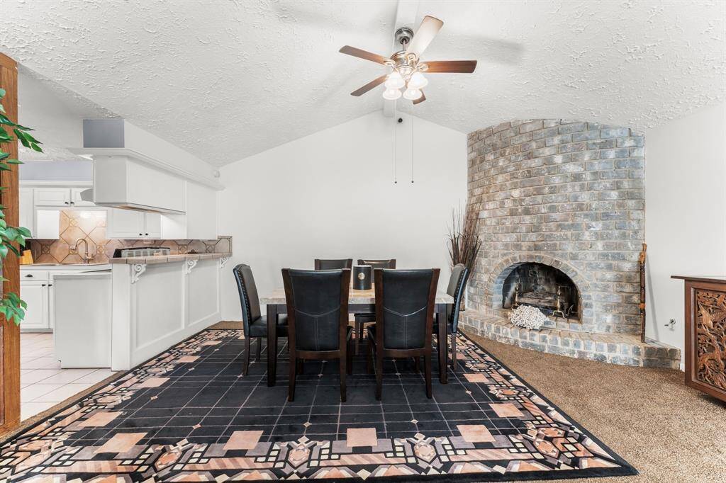 Elegant dining area featuring a unique curved brick fireplace, vaulted ceiling with fan, and a seamless flow into the open kitchen—perfect for cozy dinners and entertaining.