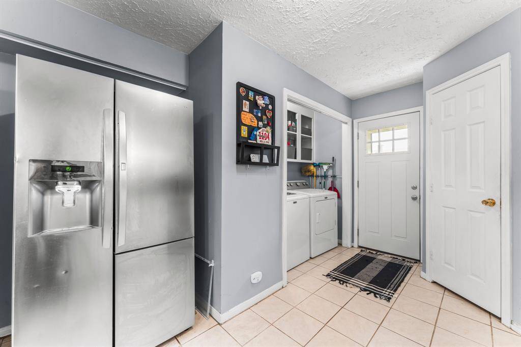 Functional utility area featuring a sleek stainless steel fridge, in-unit washer and dryer, ample storage space, and convenient access to the backyard or garage.