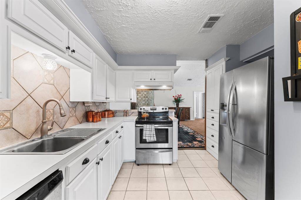 Modern gallery kitchen with crisp white cabinetry, stainless steel appliances, and a stylish tiled backsplash—flowing seamlessly into the open dining and living space.