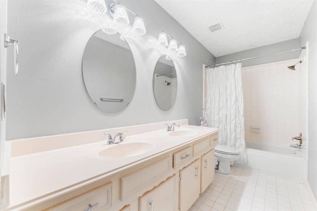 Bright and spacious full bathroom with dual sinks, elegant lighting, and a tub-shower combo—perfect for shared use or accommodating guests with ease.