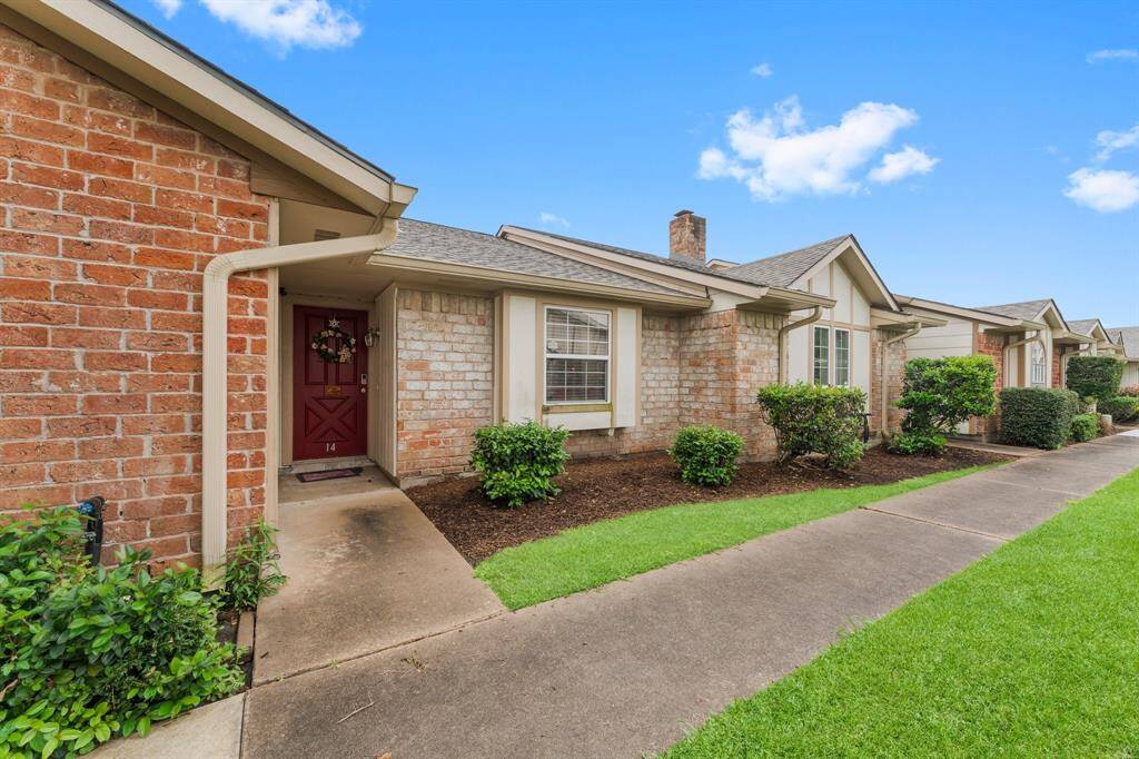 Inviting condo with a cozy red front door, brick façade, and neatly manicured landscaping in a quiet, walkable community.