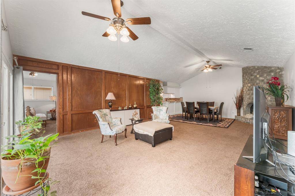Spacious living and dining area featuring high vaulted ceilings, elegant wood paneling, and a cozy stone fireplace—ready for your personal touch and furniture style.