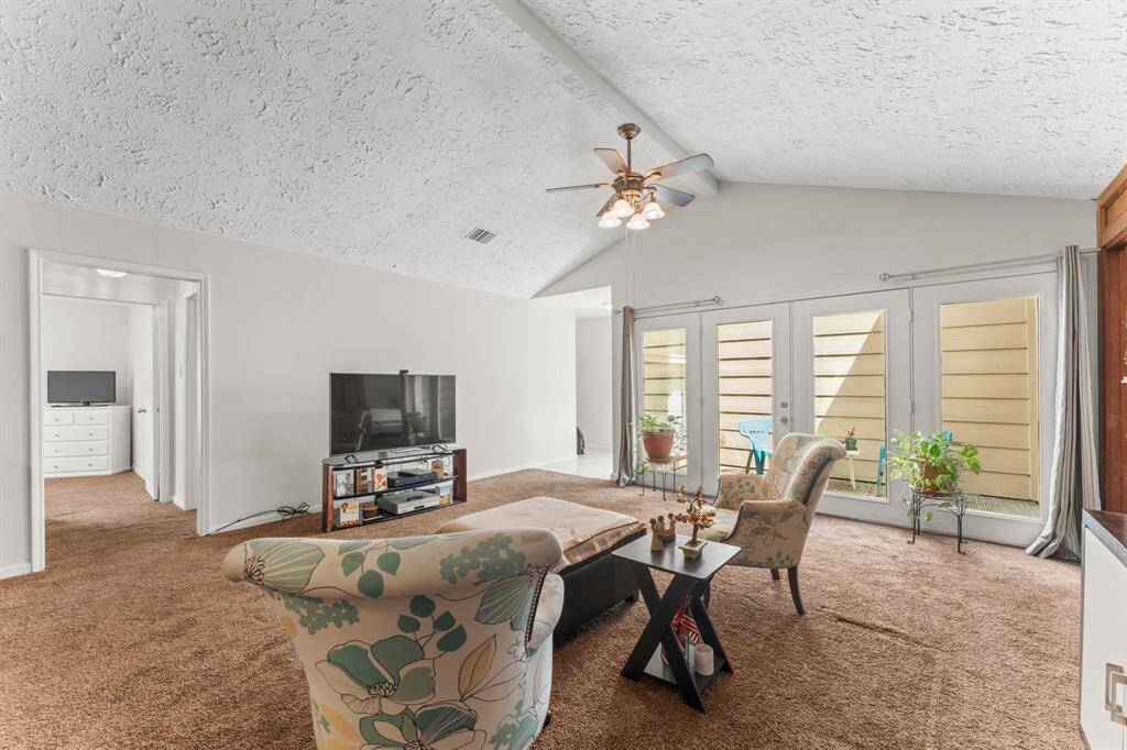 Bright and cozy living area with vaulted ceilings, plush carpeting, and large French doors that open to a private courtyard—ideal for indoor-outdoor relaxation.