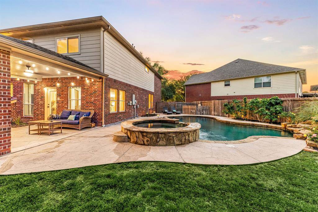 Spacious backyard with a pool and spa, surrounded by a landscaped garden. The covered patio area features cozy seating and string lights, perfect for outdoor relaxation and entertaining.