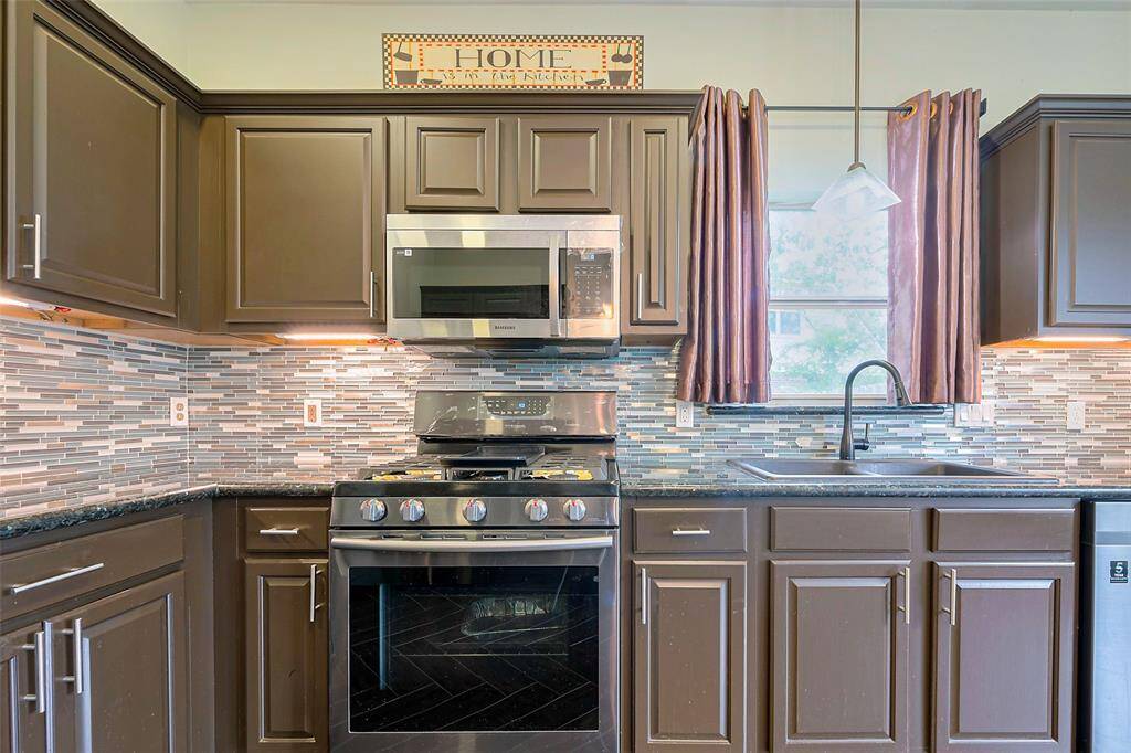 This photo features a two-story brick house with a spacious front yard and a large tree. It has a two-car garage and a covered front entryway. The property is bordered by a wooden fence and has a well-maintained lawn.