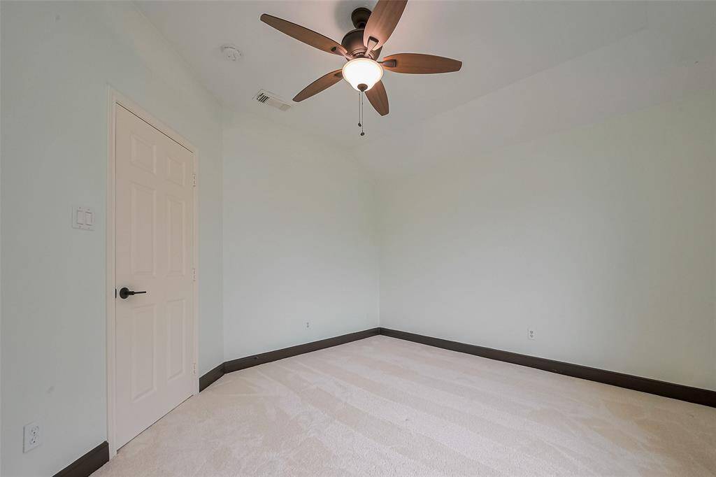 This photo showcases a bright, open living space with dark hardwood flooring and a modern chandelier. The room has a view of a staircase with a white railing and leads into a well-lit kitchen area with large windows.