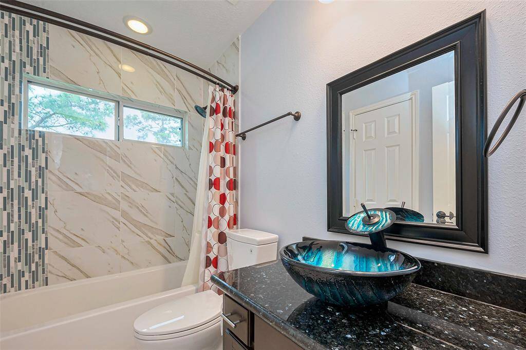 This kitchen features modern stainless steel appliances, dark wood cabinetry, and a stylish tile backsplash. The space is brightened by large windows with curtain accents and a glass door leading outside. The dark herringbone-patterned flooring adds elegance, while pendant lighting enhances the ambiance.