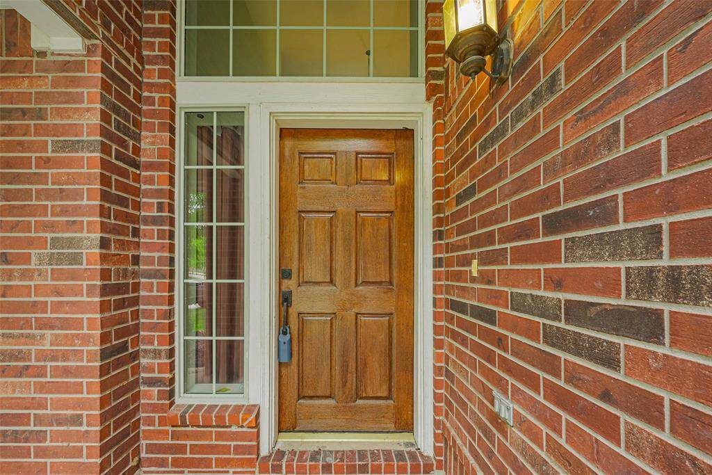 This is a two-story brick home with a spacious front yard, a two-car garage, and mature trees. The exterior features a welcoming covered entryway and a fenced backyard. Ideal for families seeking a suburban setting.