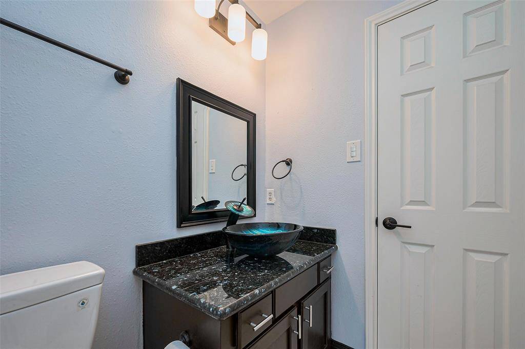This kitchen features dark cabinetry, a modern stainless steel stove and microwave, and a stylish tile backsplash. It has a window above the sink for natural light and pendant lighting for a cozy ambiance.