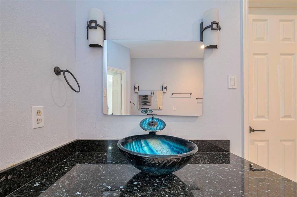 This spacious living area features high ceilings, dark wood flooring, and ample natural light from large windows. It includes a ceiling fan and tasteful wall art, offering a modern and welcoming ambiance.