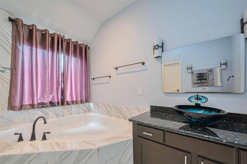 This spacious living area features high ceilings, large windows with flowing drapes, and a stylish fireplace. It seamlessly connects to an open kitchen with dark cabinetry and modern lighting, creating a bright and airy atmosphere.