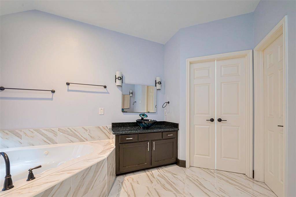 This spacious living area features high ceilings, dark hardwood floors, and a modern open layout leading to a stylish kitchen with stainless steel appliances. A balcony overlooks the room, adding an elegant touch.