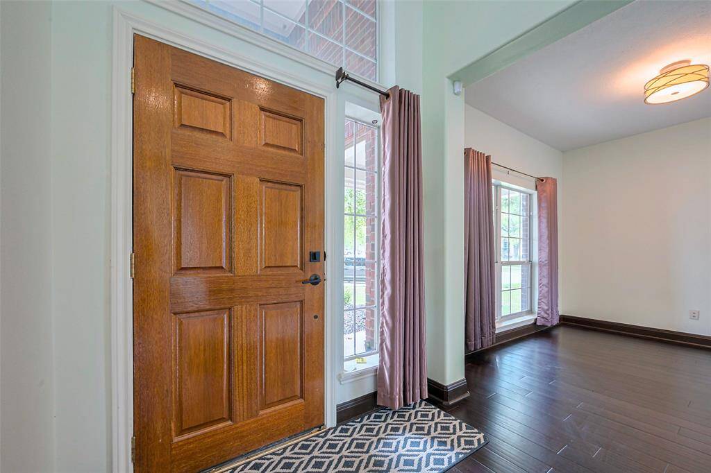 This is a two-story brick home featuring a covered entryway, large windows, and a well-maintained front yard with shrubs and a tree.
