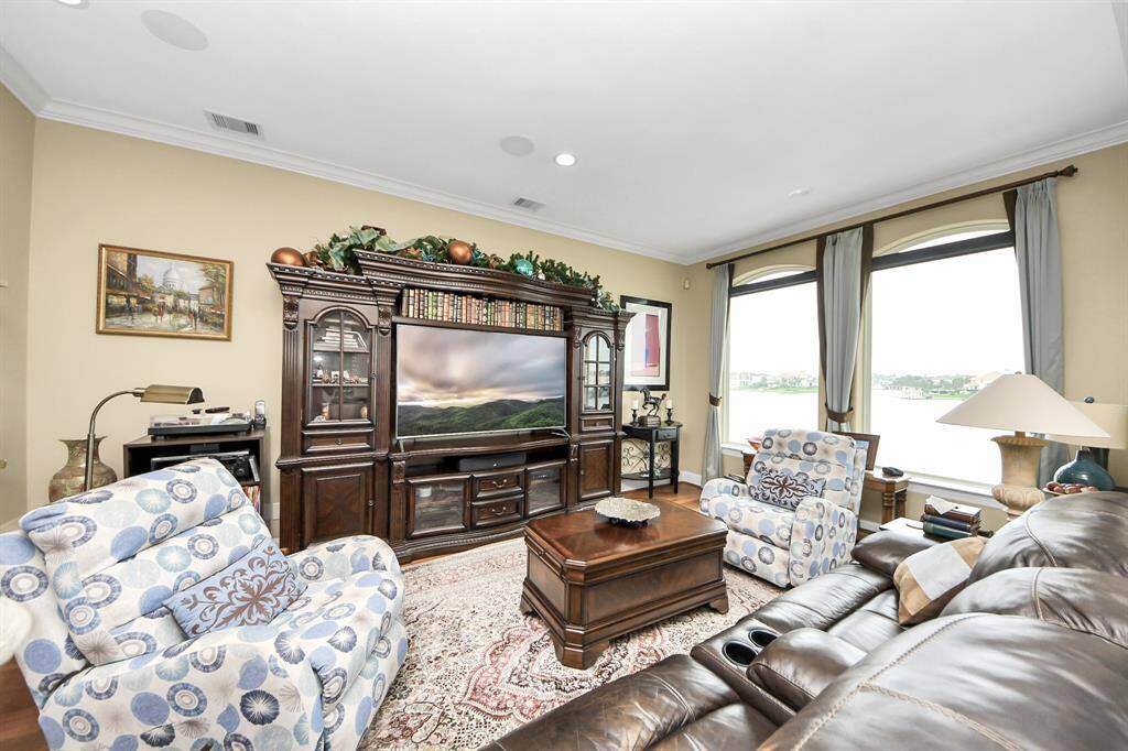This photo showcases a stylish, open-concept living area with hardwood floors, featuring a cozy dining nook, a built-in wet bar with glass cabinets, and a built in beverage cooler. The large windows offer abundant natural light and lake views, in addition to the double doors that lead to the outdoor 2nd floor patio sitting area.