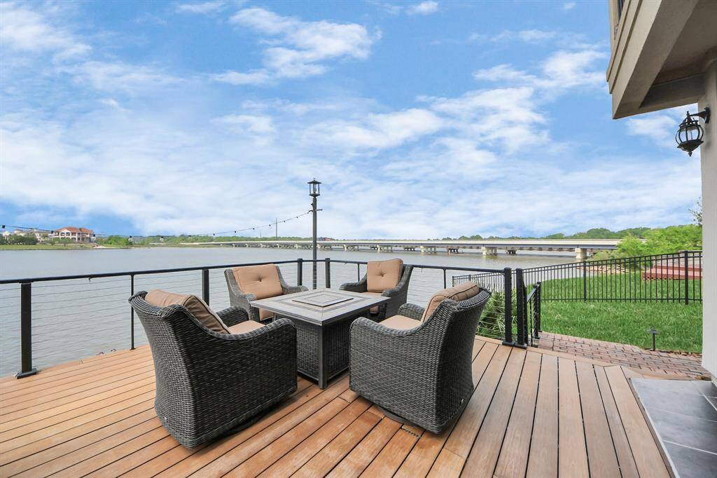This photo showcases a spacious waterfront deck with comfortable outdoor seating, a fire pit table, and a barbecue grill. It offers stunning views of a serene body of water, perfect for relaxation and entertaining.