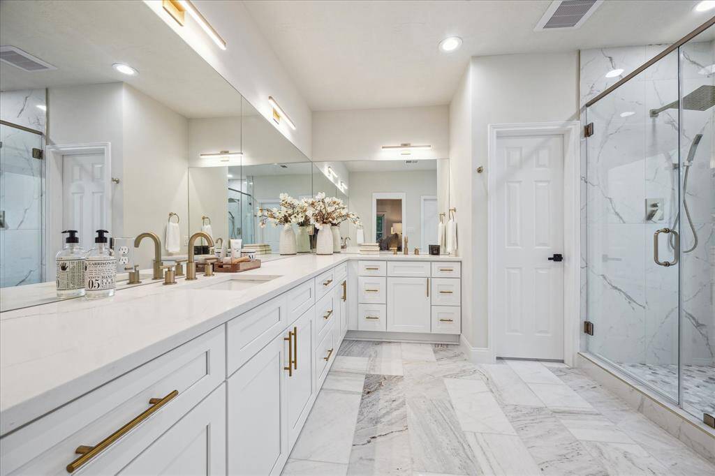 The primary bath retreat offers a spa-like experience, featuring oversized vanity spaces with beautiful countertops that exude elegance. Designer fixtures add a sophisticated touch, while the abundance of storage space ensures everything has its place. The room is further elevated with luxurious marble tile floors, creating a timeless and polished look. This meticulously designed bathroom offers both function and beauty, making it the perfect place to relax and indulge.
